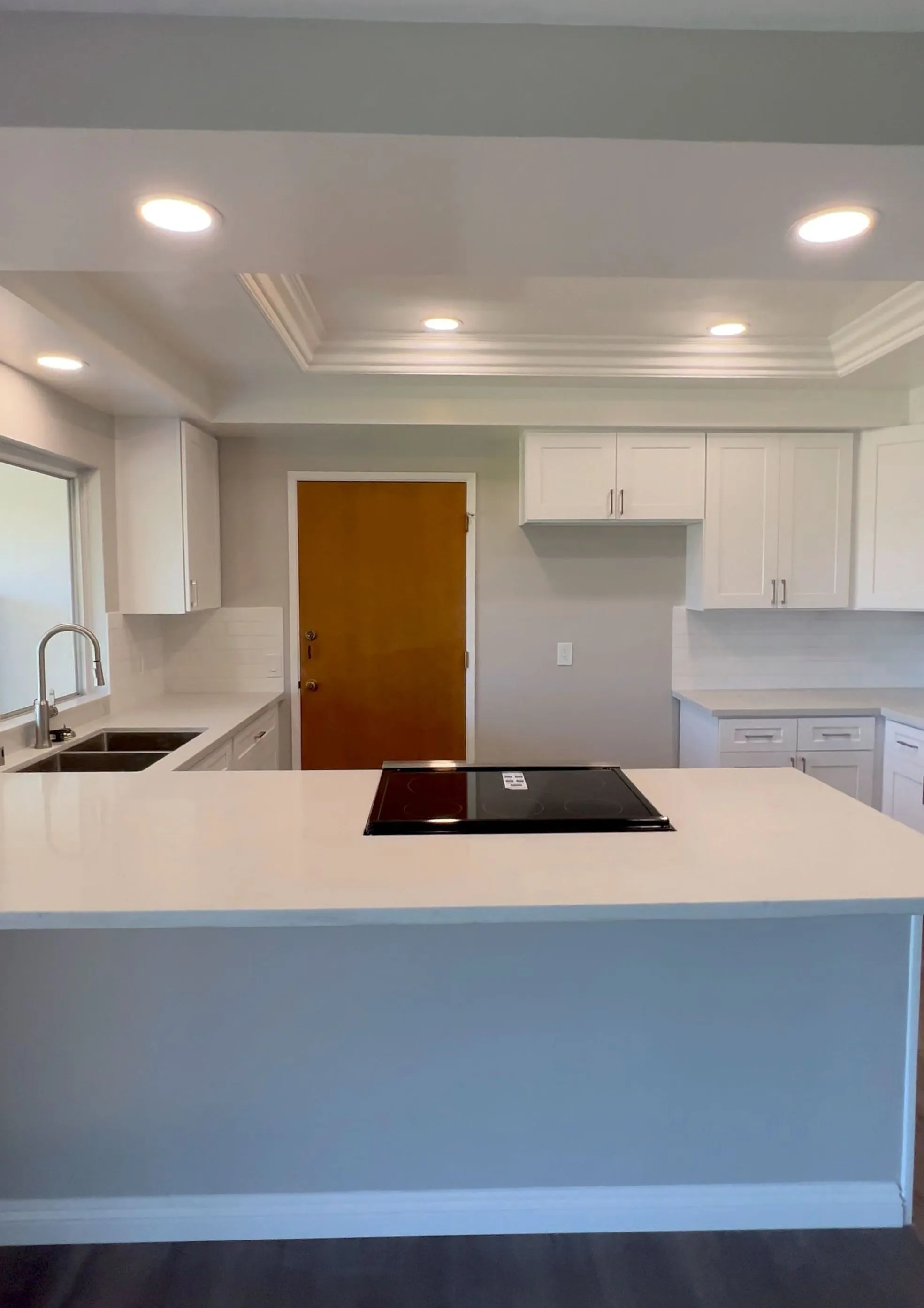 NewGen kitchen remodel with white shaker cabinets, quartz island and cooktop